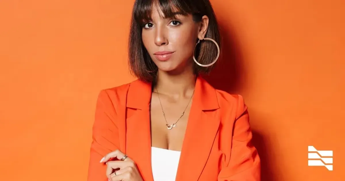 Confident freelance professional in a vibrant orange blazer, embodying the ambition required to secure a first client.