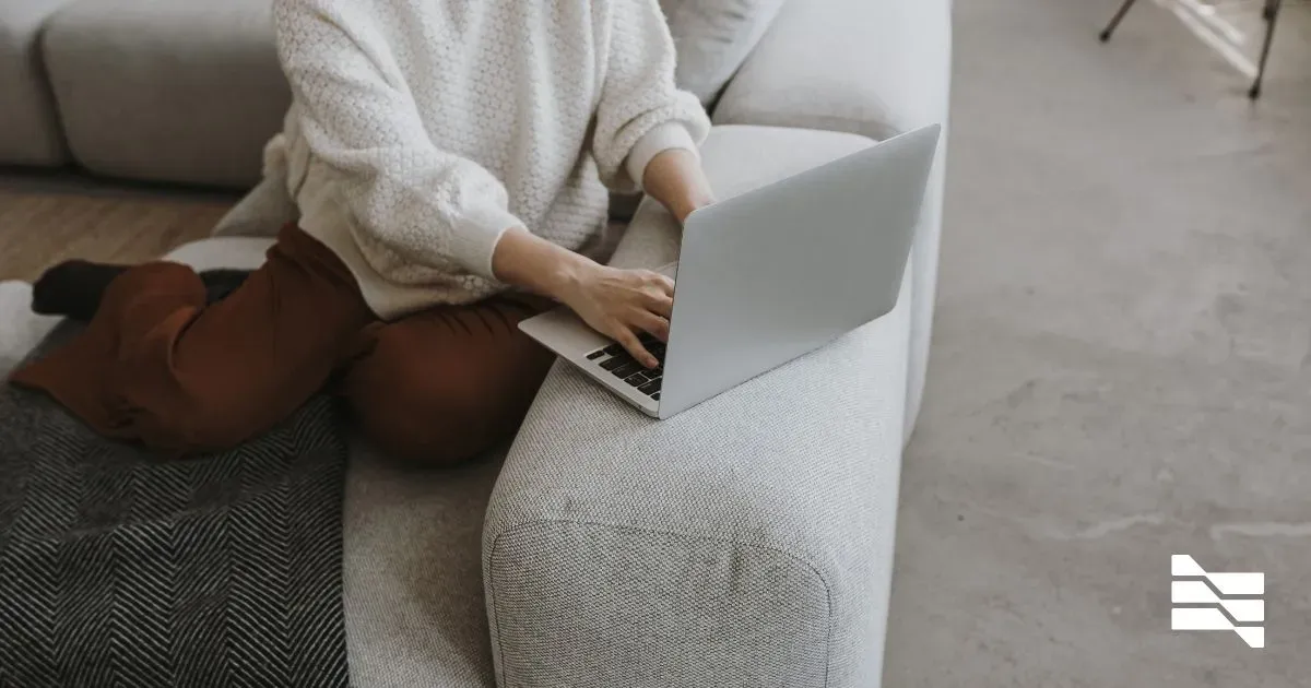 Person in a cozy sweater working on a laptop on a sofa, embodying the focused comfort necessary to maximize productivity when working from home.